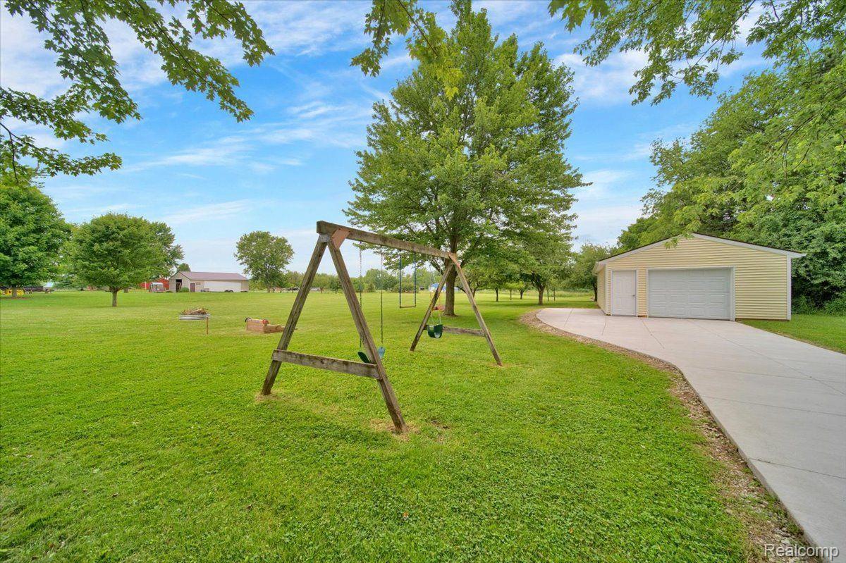 Spacious lawn with a wooden swing set, mature trees, and a detached garage.