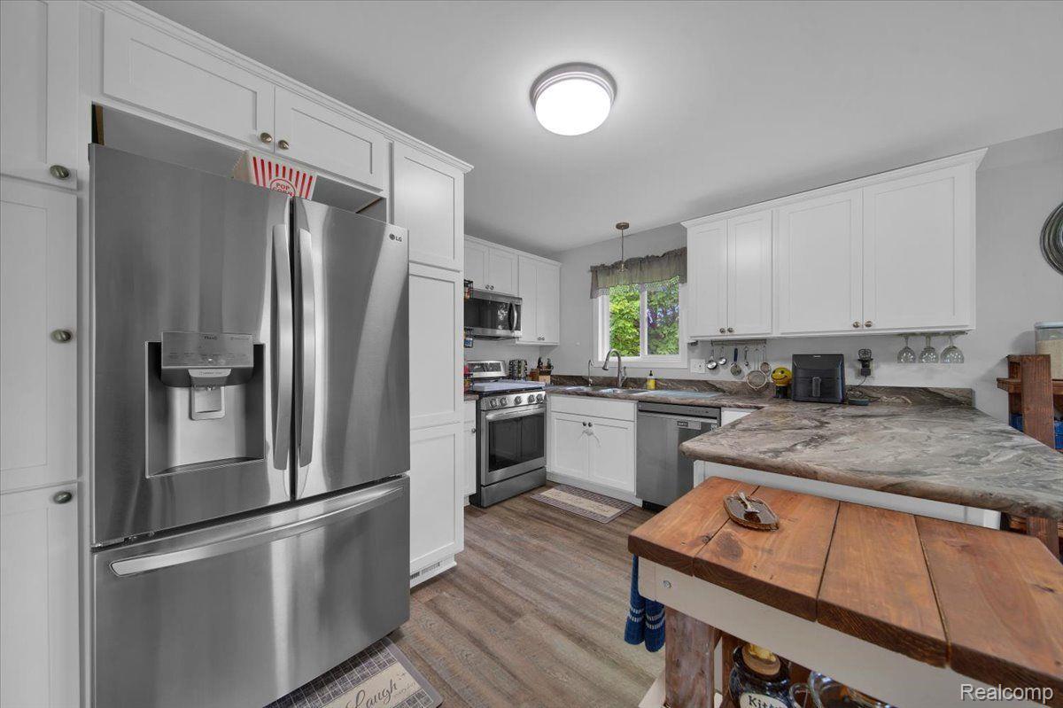 Kitchen with white cabinets, stainless steel appliances, stone counters, and a wooden island table.