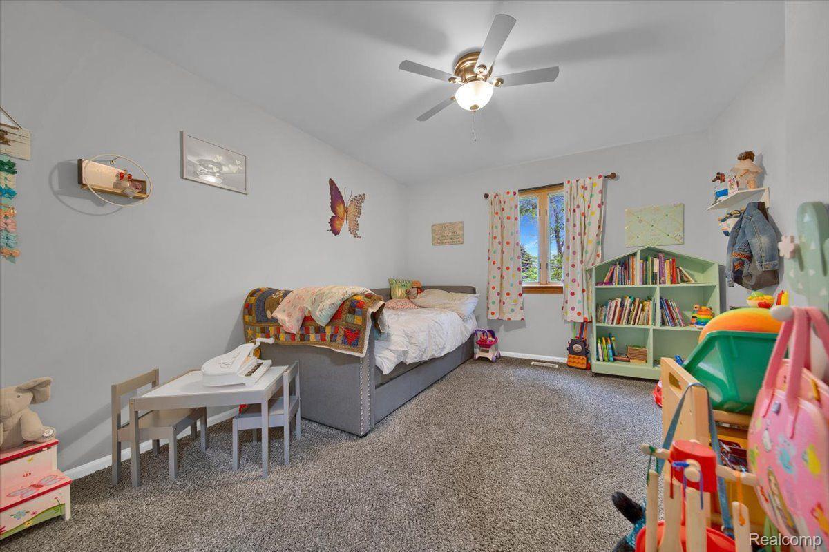 Furnished bedroom with a bed, colorful curtains, children's bookshelves, and toys.