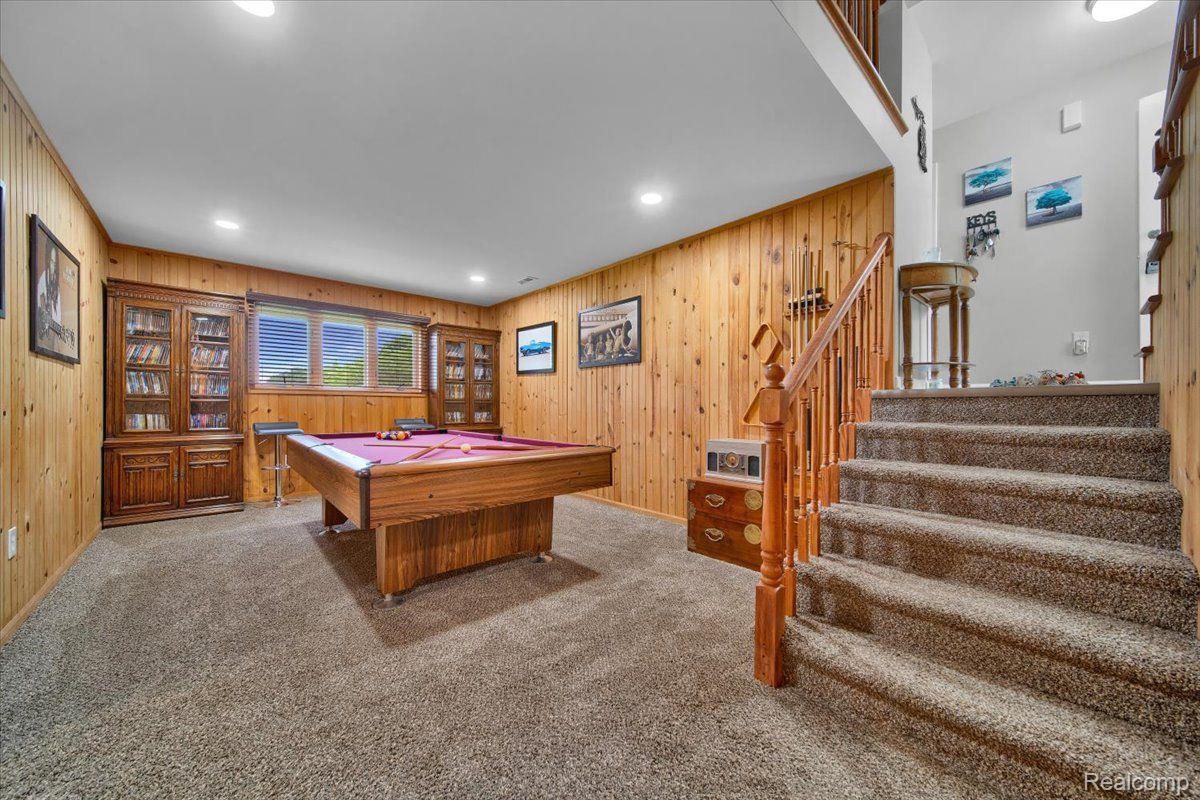 Basement recreation room with a pool table, wood-paneled walls, and carpeted stairs.