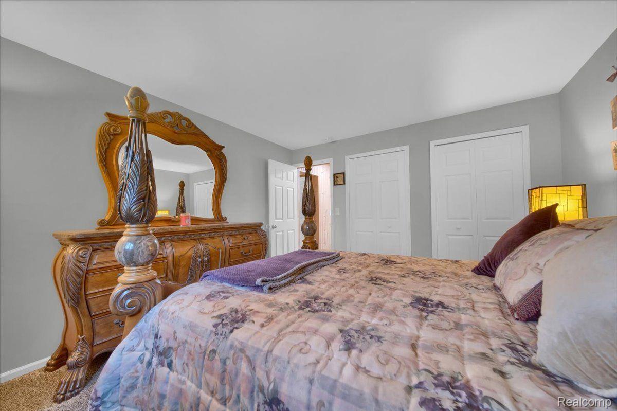 Furnished bedroom with a floral quilt and an ornate carved wooden dresser and mirror.