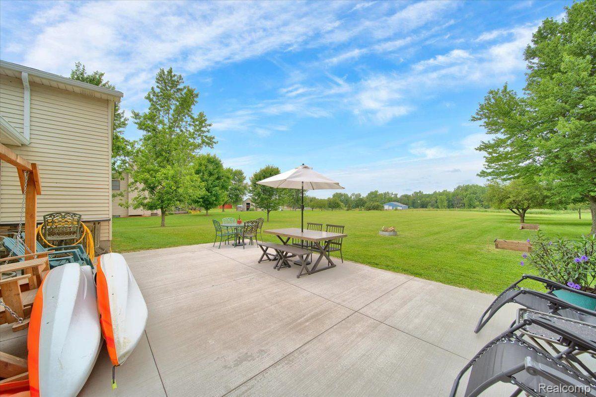 Backyard patio with umbrella-covered dining tables, kayaks, and a broad tree-lined lawn.