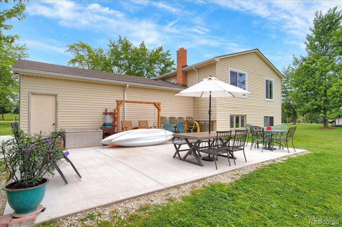 Rear of a beige two-story home with a furnished patio, white umbrella, and kayak.