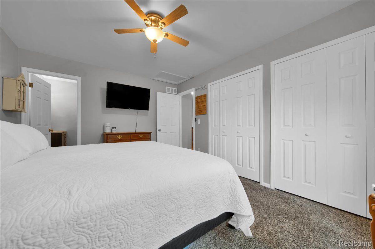 Bedroom with a large white-quilted bed, wooden-blade ceiling fan, and several white closet doors.