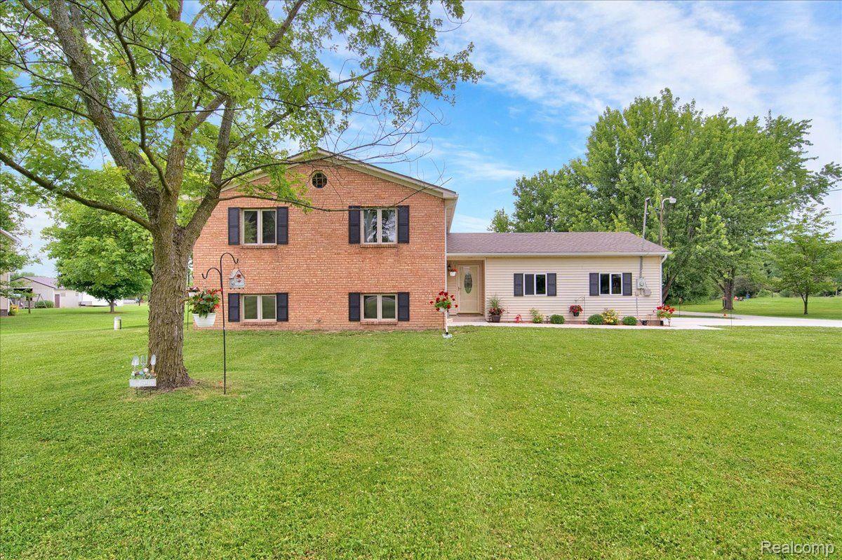 Brick split-level home with a beige wing, flower beds, and a broad lawn beneath mature trees.