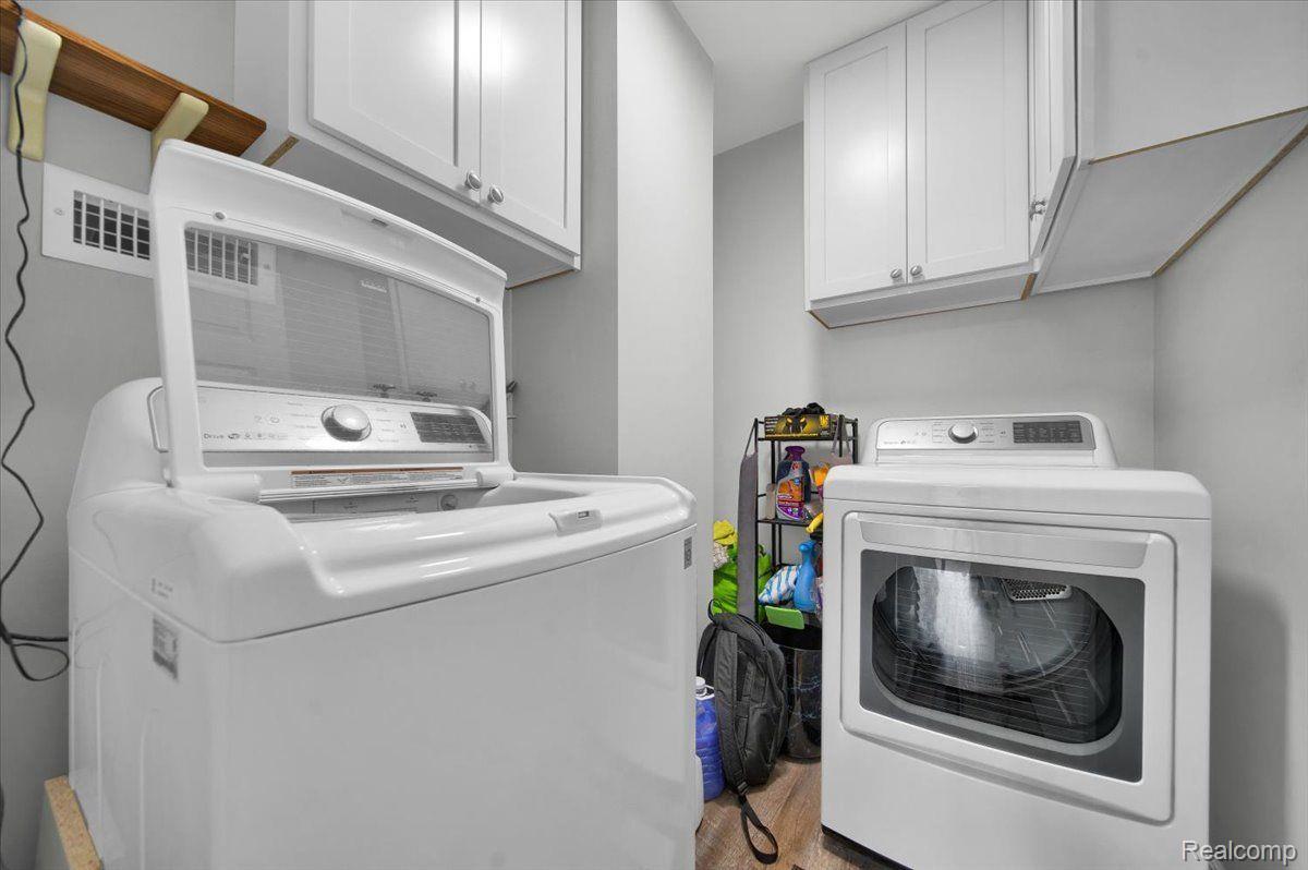 Laundry room with a top-loading washer, front-loading dryer, and overhead storage cabinets.