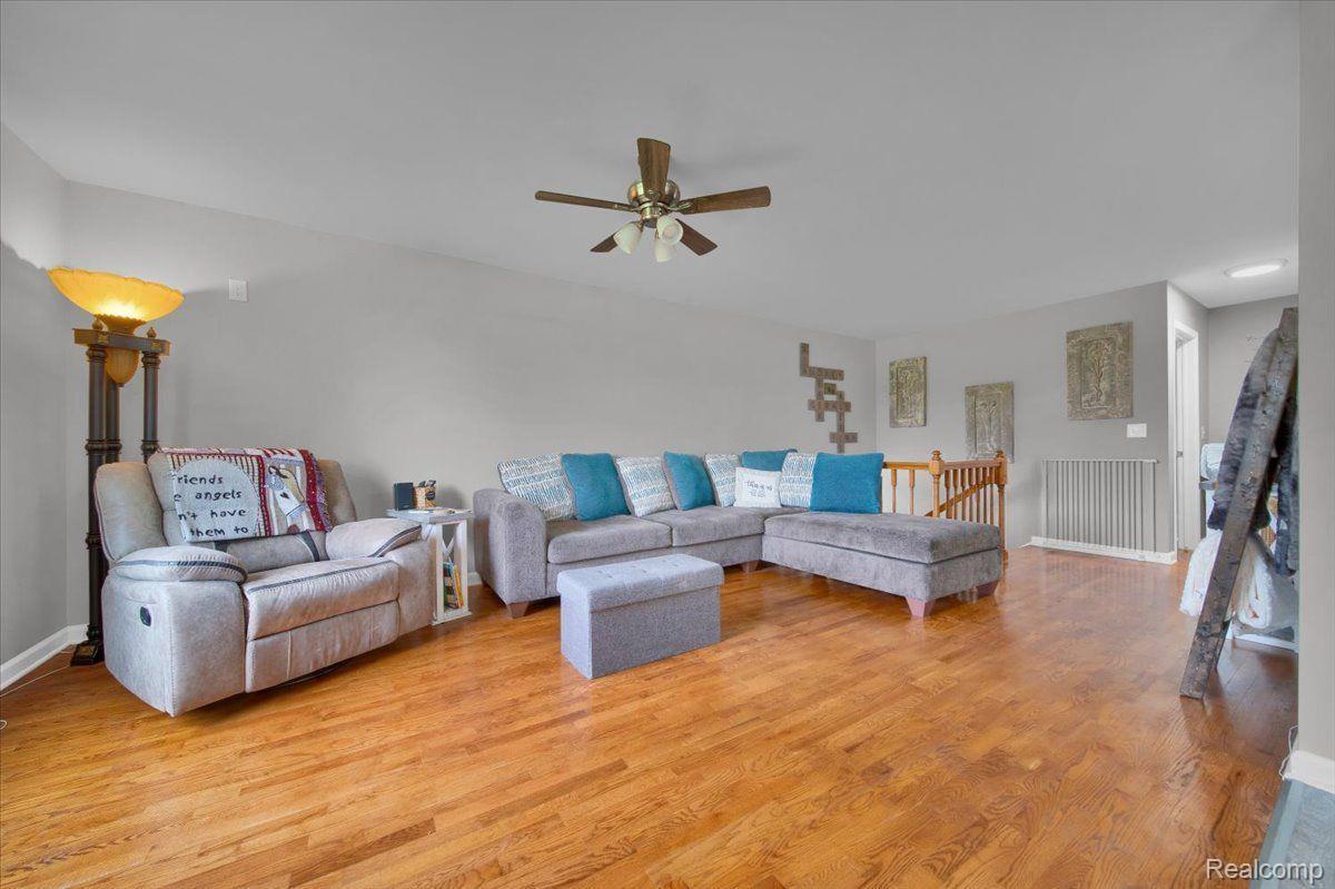 Furnished living room with gray sectional seating, hardwood floors, and a ceiling fan.