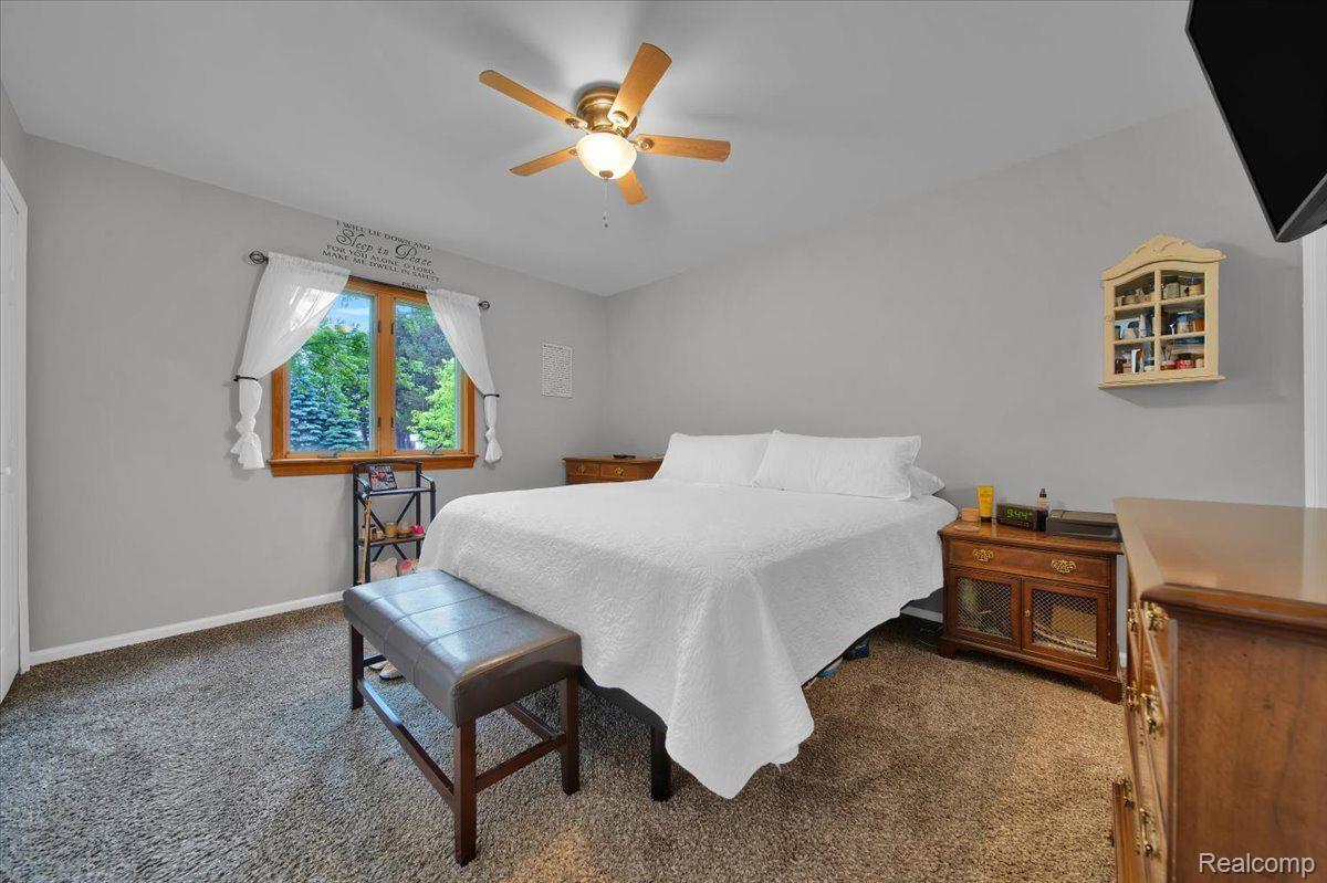 Bedroom with a white bed, gray bench, wood-framed window, and wooden dressers.