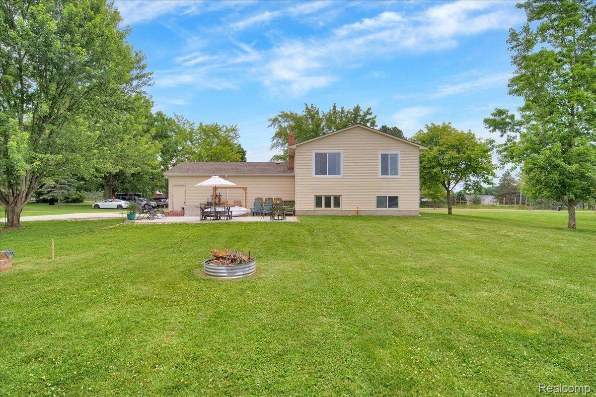 Beige two-story home with a patio, broad lawn, and metal fire pit in the foreground.