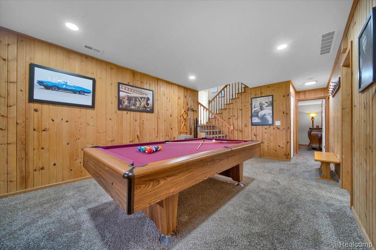 Basement game room with a large pool table, wood-paneled walls, and gray carpeting.