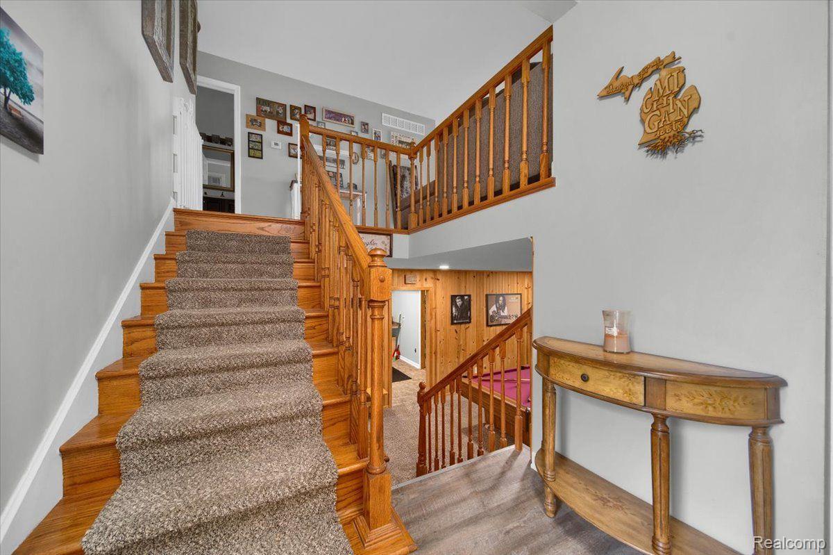 Foyer with a carpeted staircase, wood railings, upper landing, and curved console table.