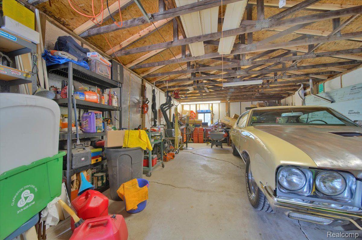 Garage with exposed roof trusses, crowded storage shelves, and a cream-colored classic car.