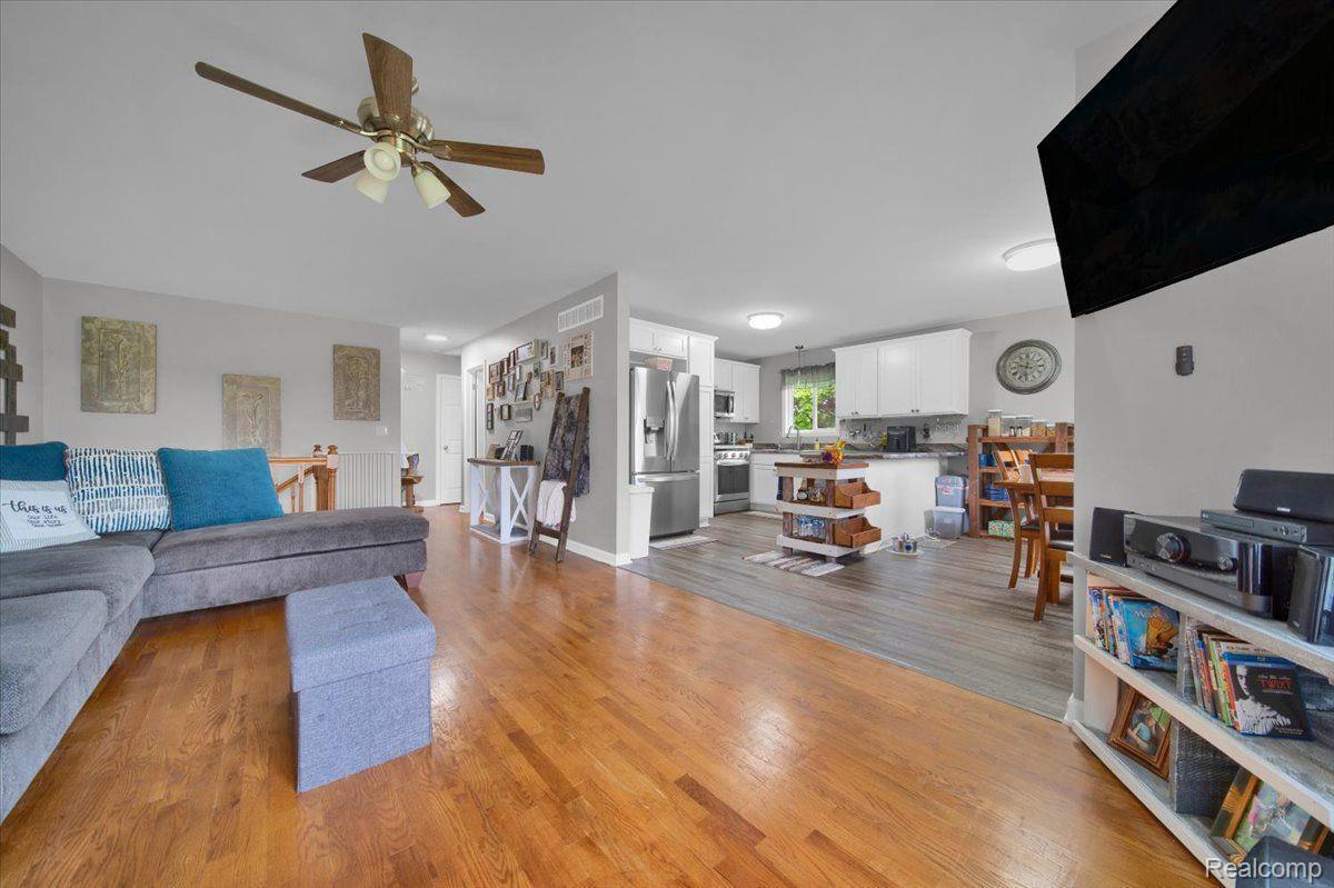 Open living room and kitchen with hardwood floors, gray sectional, white cabinets, and stainless steel appliances.