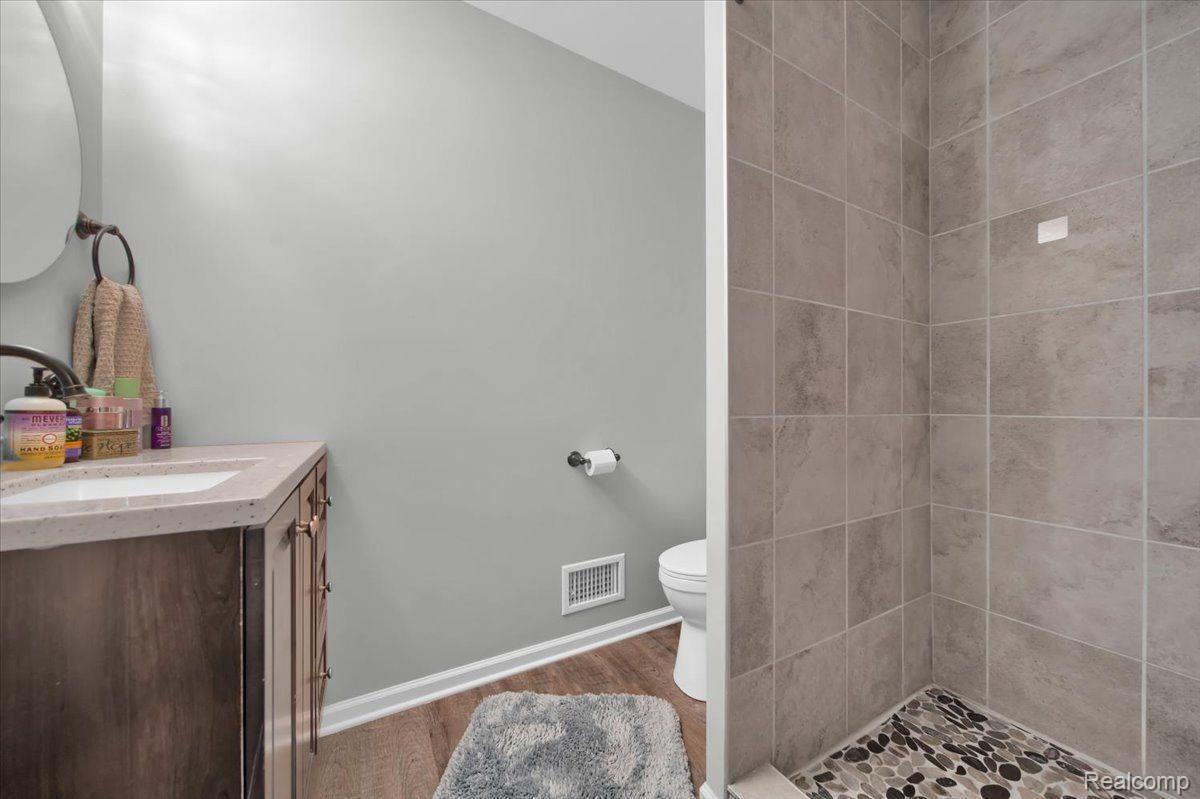 Bathroom with a wood vanity, toilet, and tiled walk-in shower with pebble flooring.