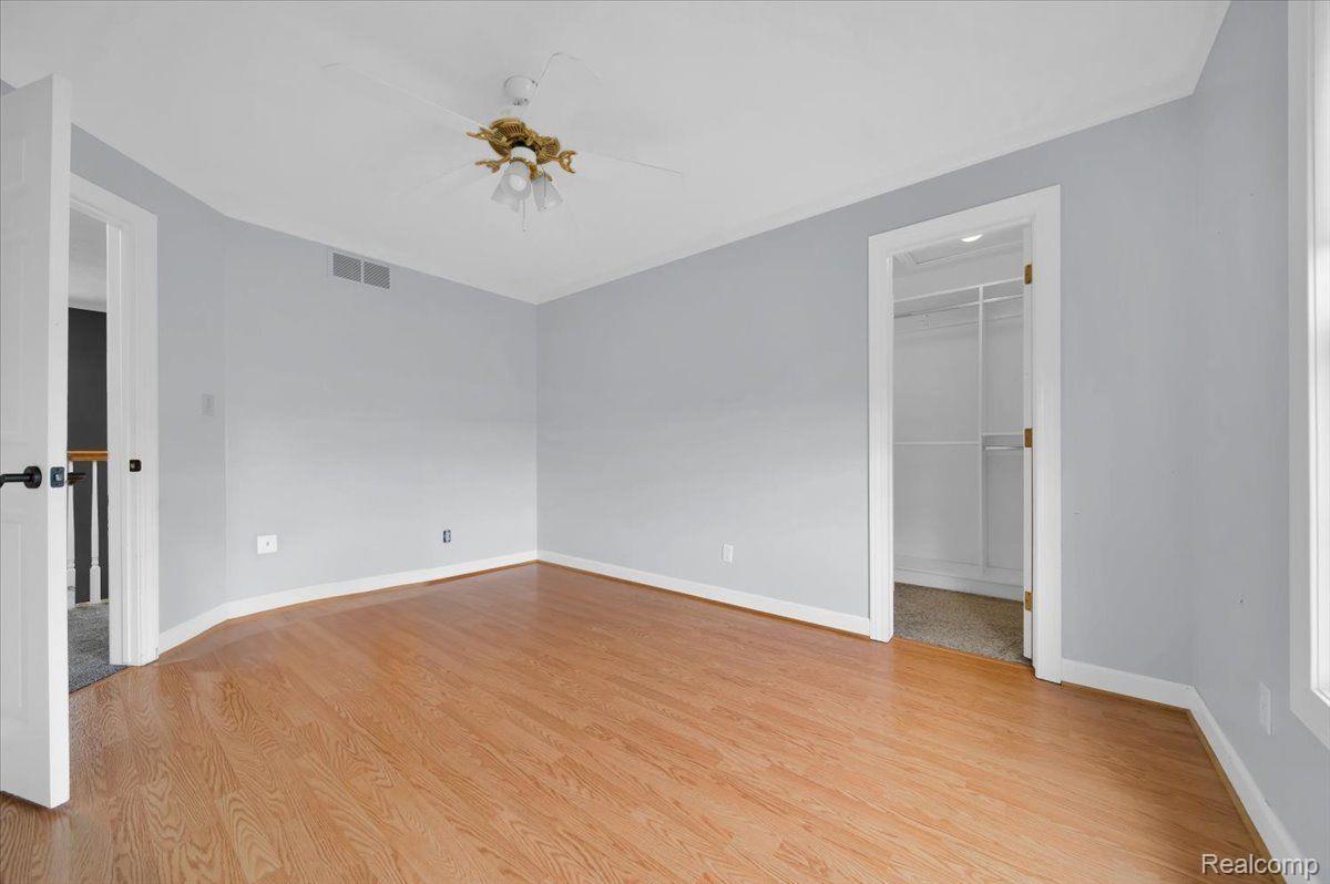 Empty bedroom with hardwood floors, a ceiling fan, and an open closet doorway.
