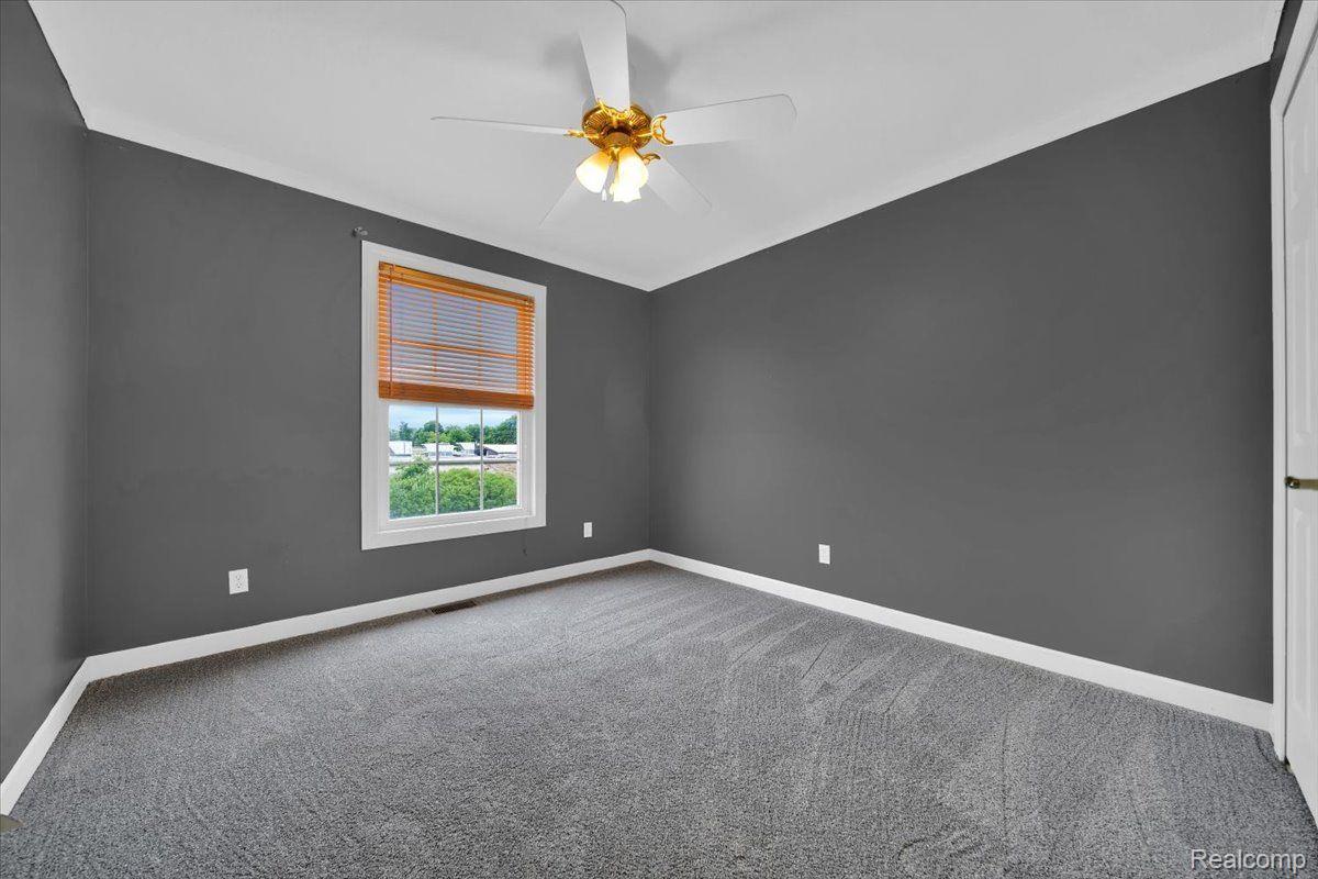 Empty bedroom with gray walls and carpet, a ceiling fan, and a window with wooden blinds.