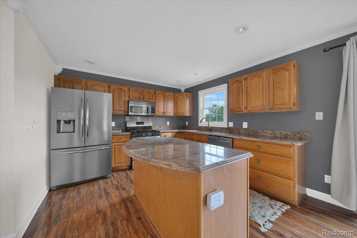 Kitchen with wood cabinets, granite island, stainless steel appliances, and dark gray walls.