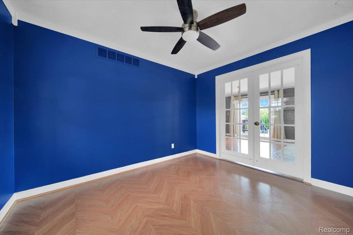 Empty blue-walled room with herringbone flooring, a ceiling fan, and white French doors.