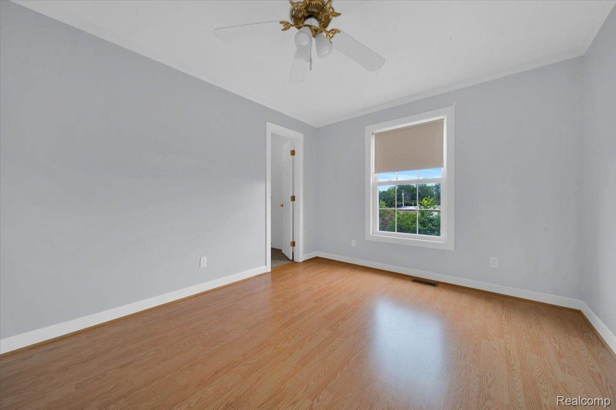 Empty bedroom with wood-look flooring, gray walls, a window, and a ceiling fan.