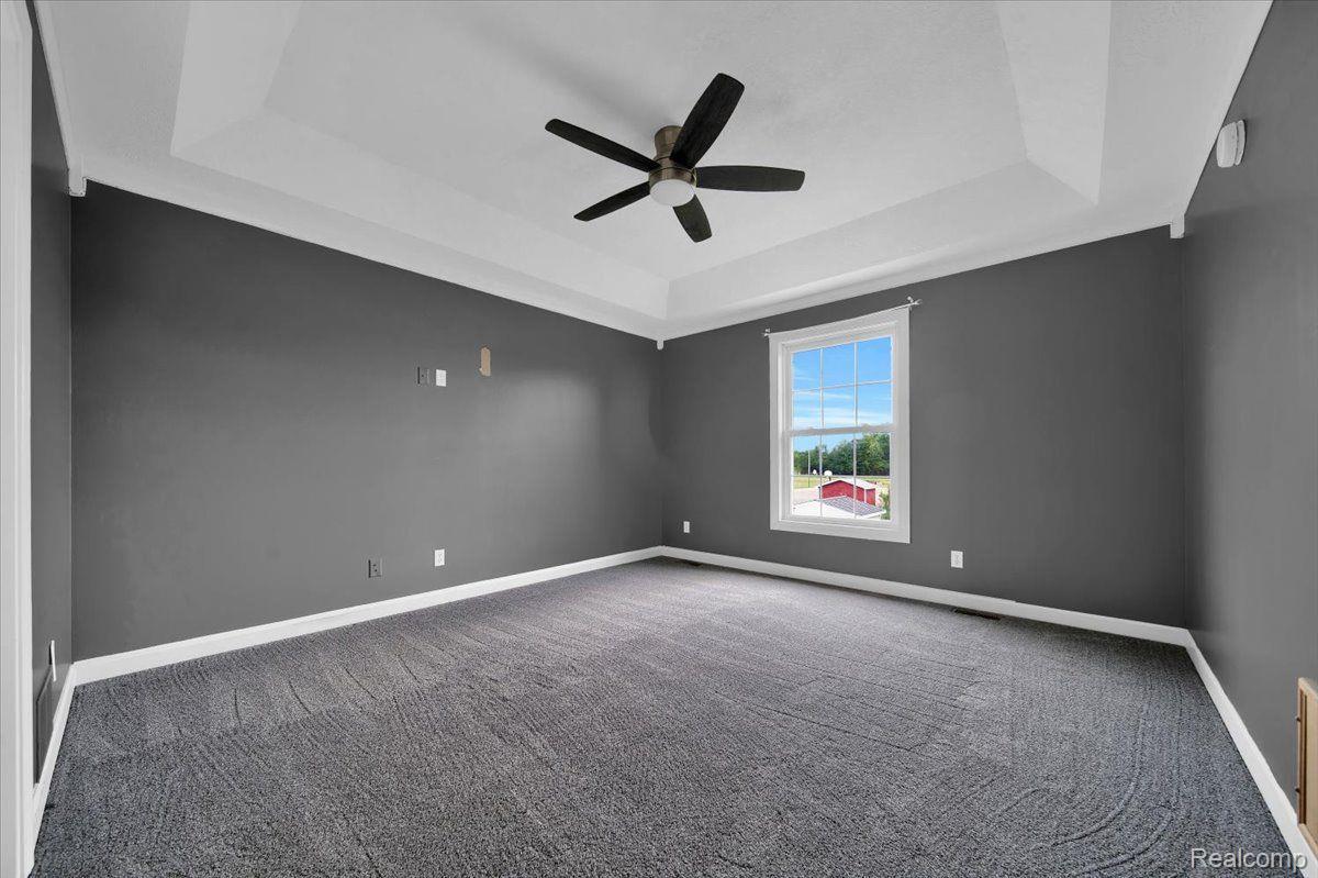 Vacant bedroom with gray carpet, a tray ceiling, black fan, and a window overlooking trees.