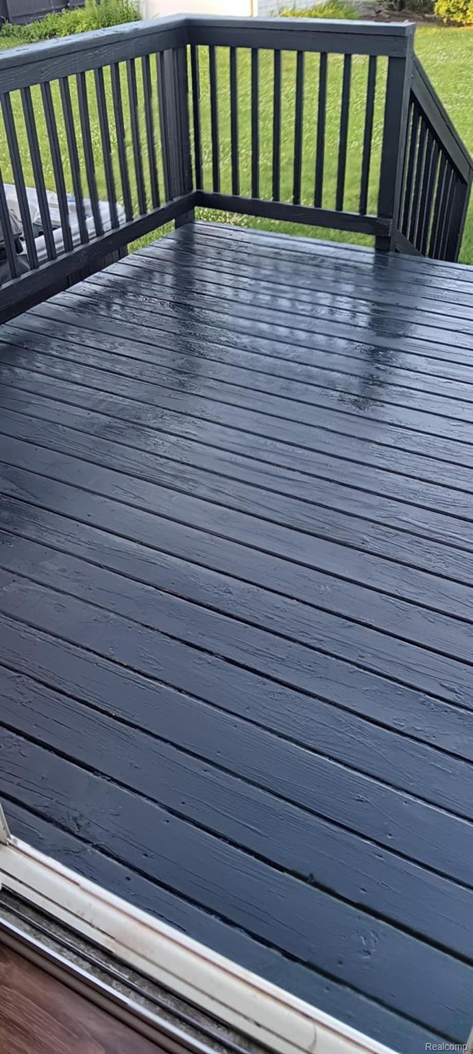 Wet dark-painted wooden deck with matching railings overlooking a green lawn.
