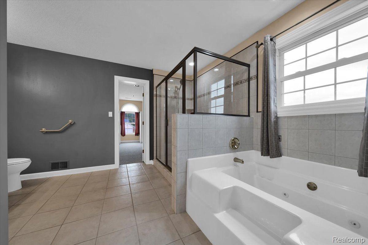 Bathroom with a jetted corner tub, glass shower, large window, and grab bar.