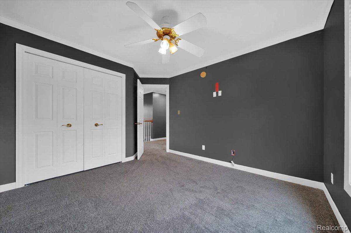 Vacant bedroom with gray carpet, charcoal walls, double closet doors, and a ceiling fan.