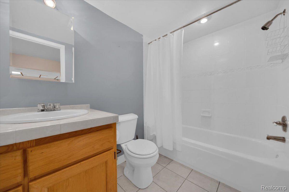 Bathroom with a wood vanity, toilet, and white tub-shower with curtain.