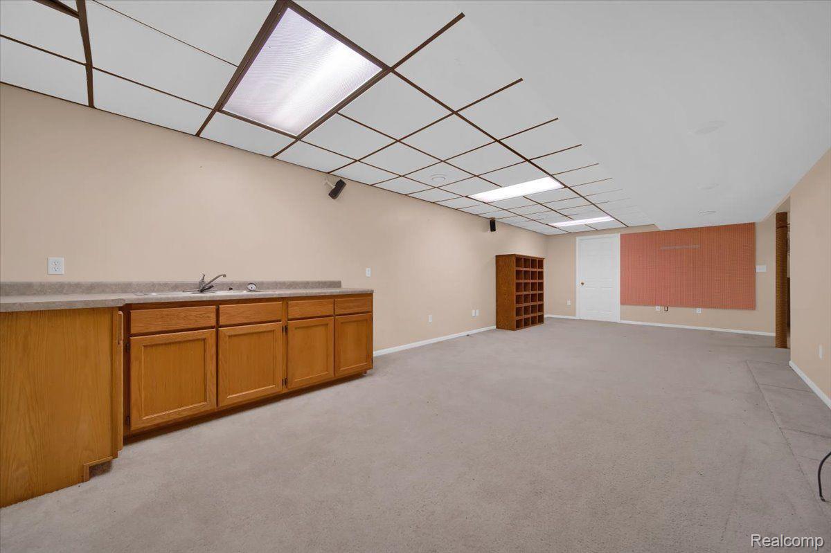 Basement recreation room with a wooden wet bar, beige carpet, and a fluorescent-lit drop ceiling.