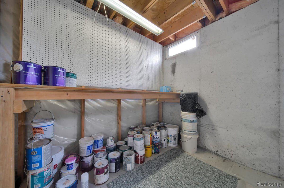 Basement storage area with a pegboard wall, wooden shelf, and many paint cans.