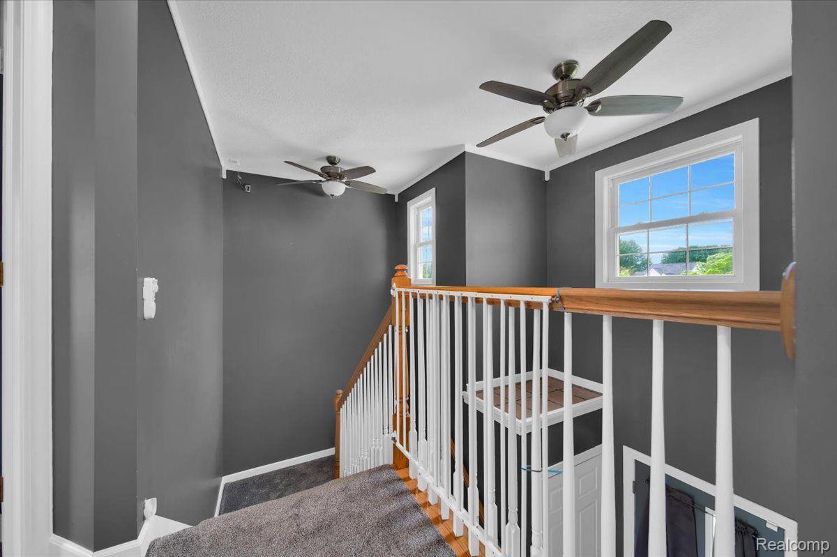 Upstairs stair landing with gray walls, carpeted stairs, wood handrail, and two ceiling fans.