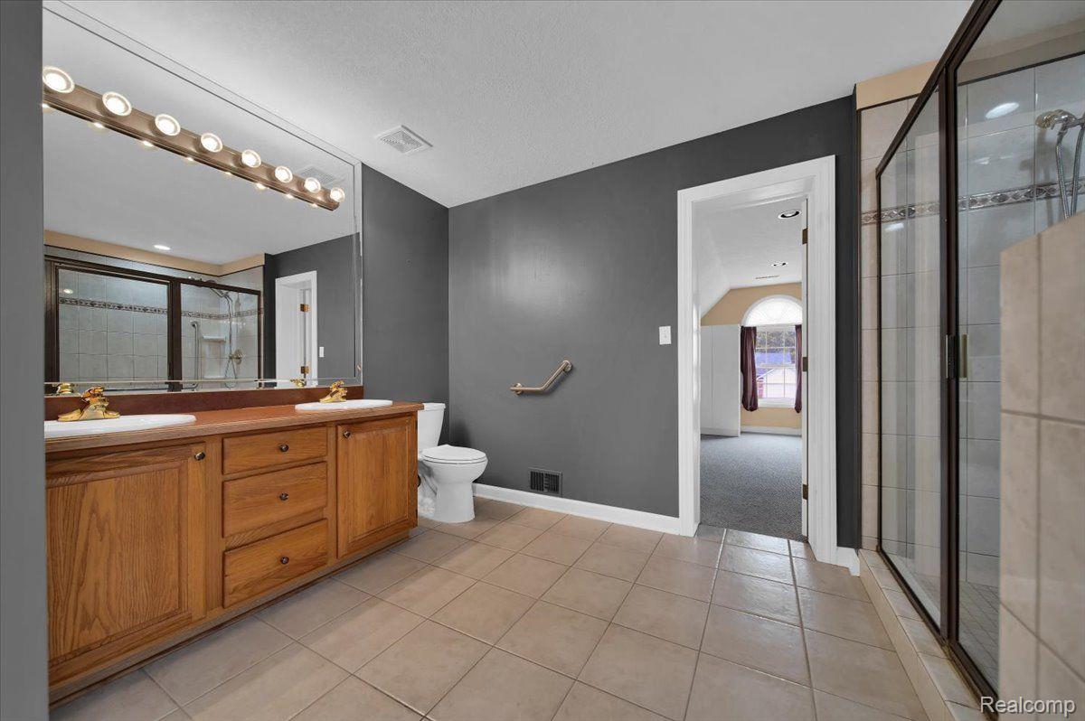 Bathroom with a wooden double vanity, large mirror, and glass-enclosed tiled shower.