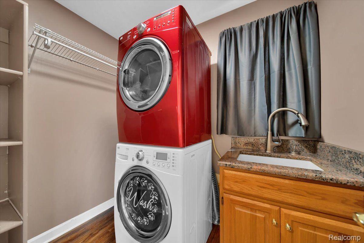 Laundry room with stacked red and white washer and dryer beside a granite-topped utility sink.