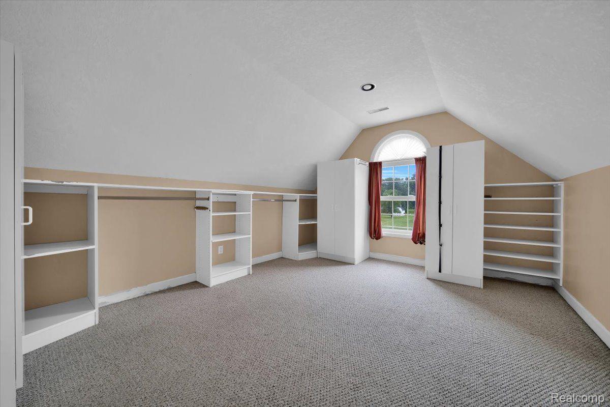 Carpeted room with sloped ceilings, built-in shelving, and a curtained window.