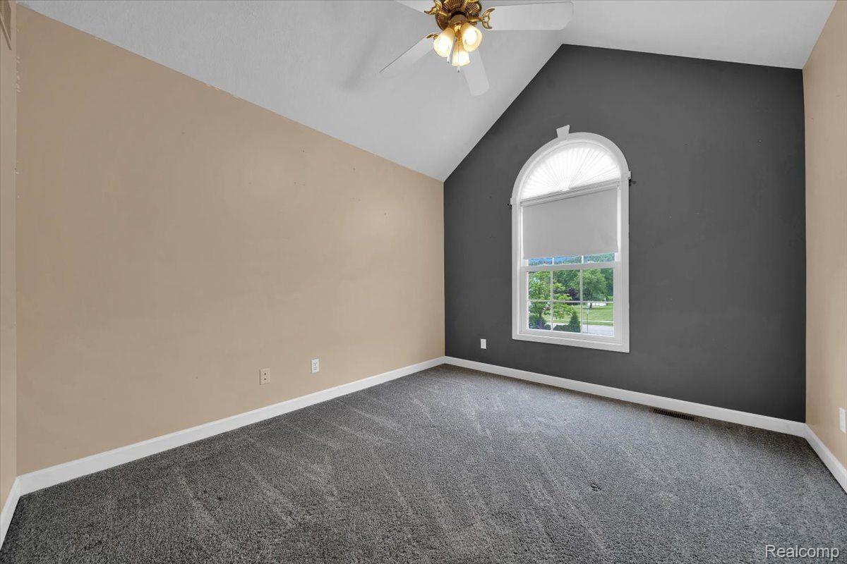 Empty carpeted room with a vaulted ceiling, gray accent wall, and arched window.