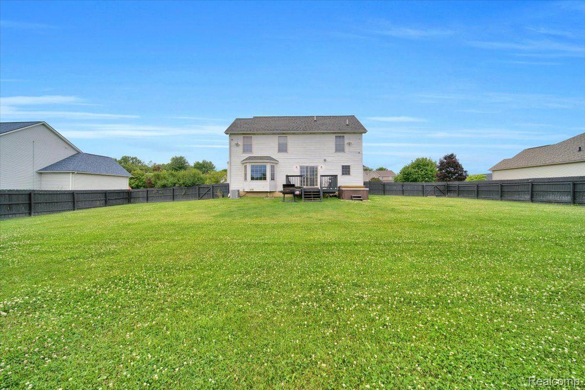 Rear of a two-story house beyond a broad fenced lawn, with a small deck.