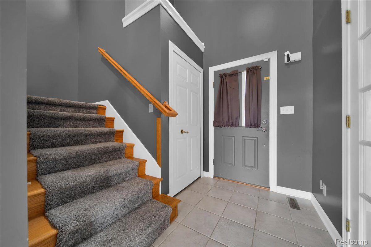 Entryway with a carpeted staircase, tiled floor, and gray front door.