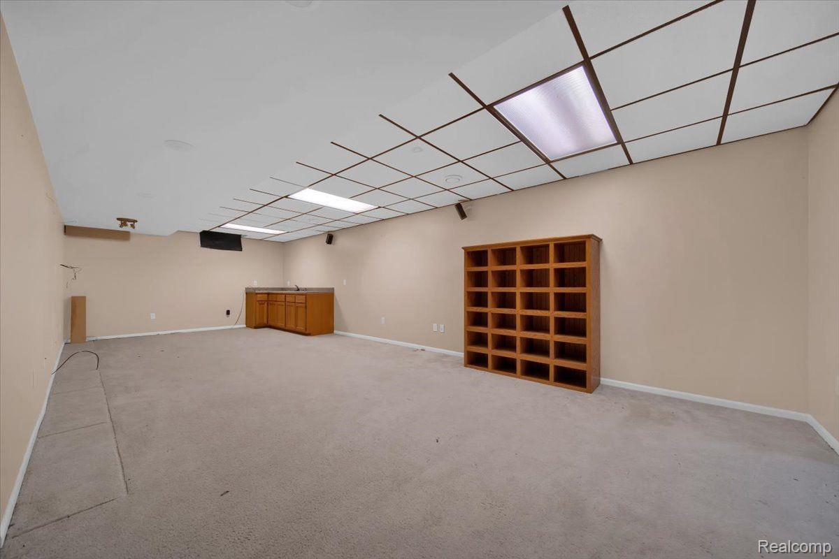 Carpeted recreation room with a drop ceiling, wooden counter, and freestanding bookcase.