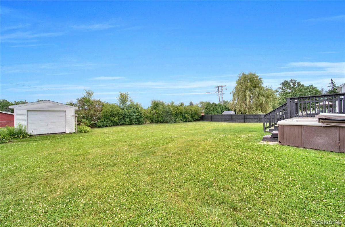 Spacious grassy backyard with a white shed, fenced yard, raised deck, and hot tub.