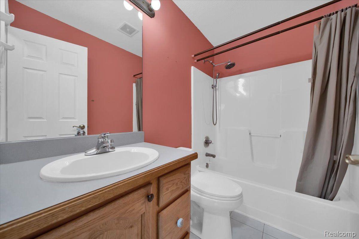 Bathroom with a wood vanity, white sink, and tub-shower against coral-pink walls.