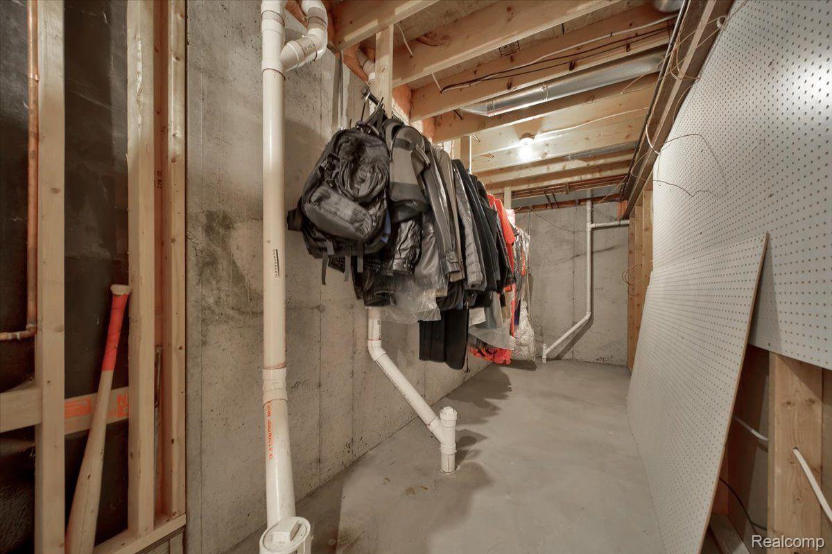 Unfinished basement storage area with exposed pipes, hanging coats and bags, and a leaning pegboard.