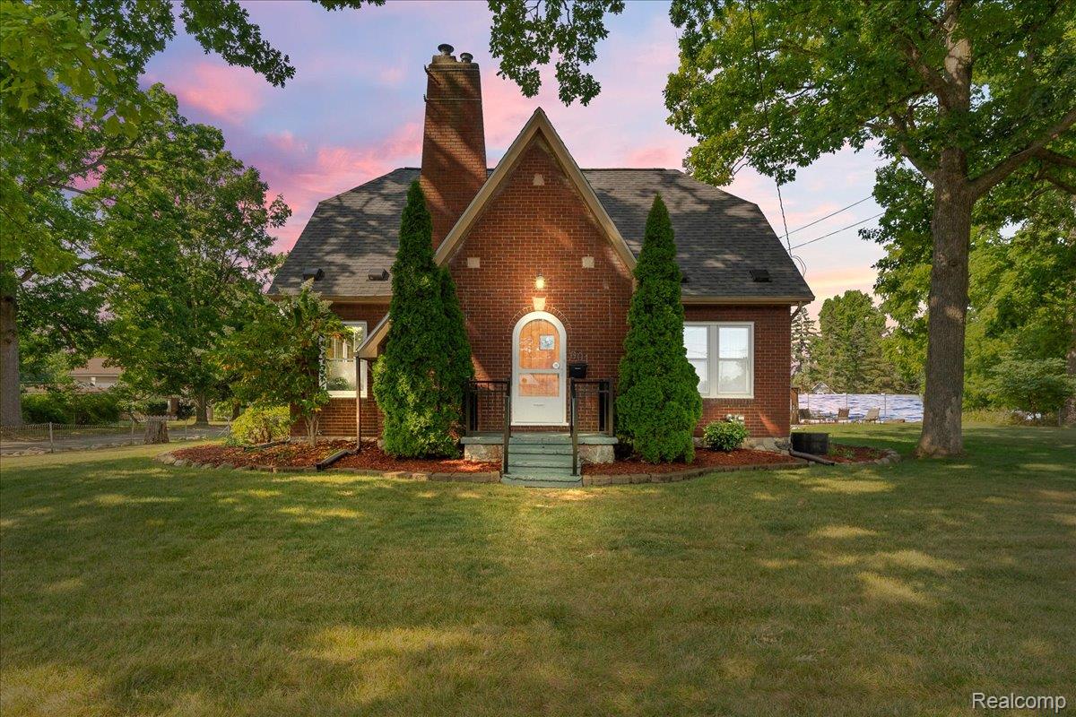 Brick house with a steep gabled roof and central entry, framed by trees at sunset.