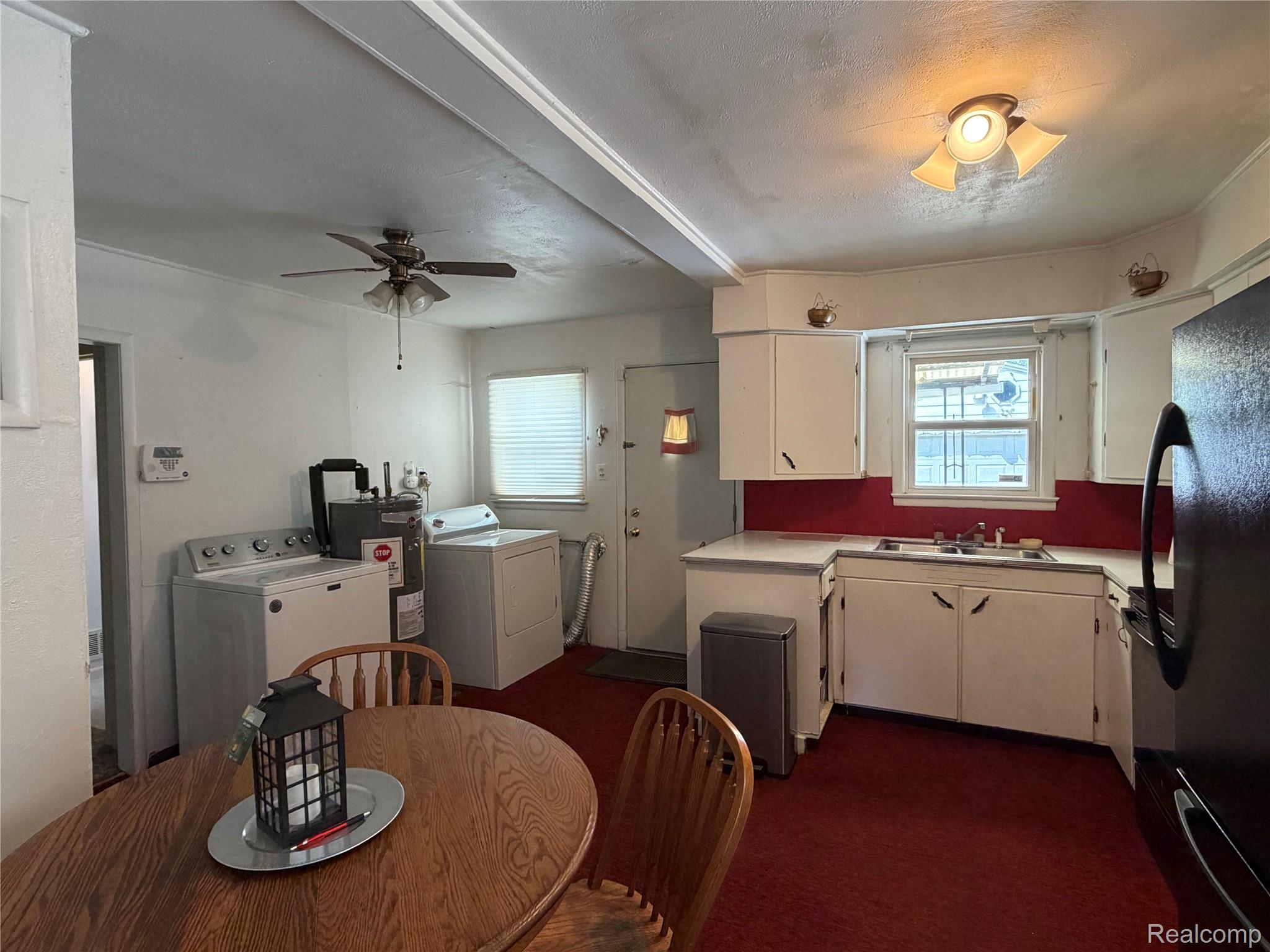 Kitchen and laundry area with white cabinets, red backsplash, washer and dryer, and a wooden dining table.