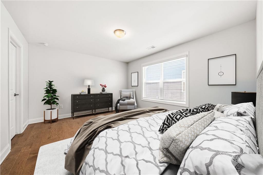 Staged bedroom with patterned white bedding, a dark dresser, wood floors, and a wide window with blinds.