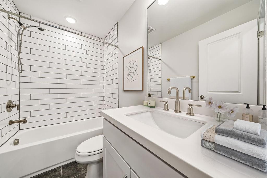 Bathroom with a white subway-tile tub and shower beside a wide vanity with a large mirror.