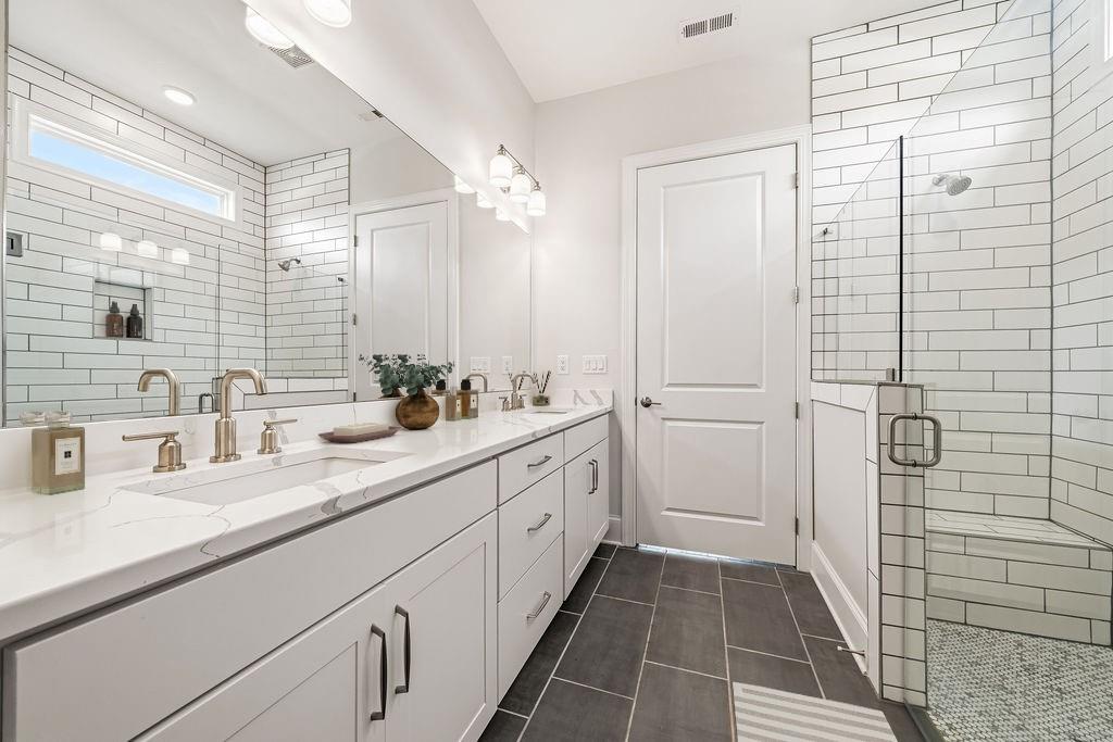 Bathroom with a long double-sink vanity and glass shower with built-in bench.