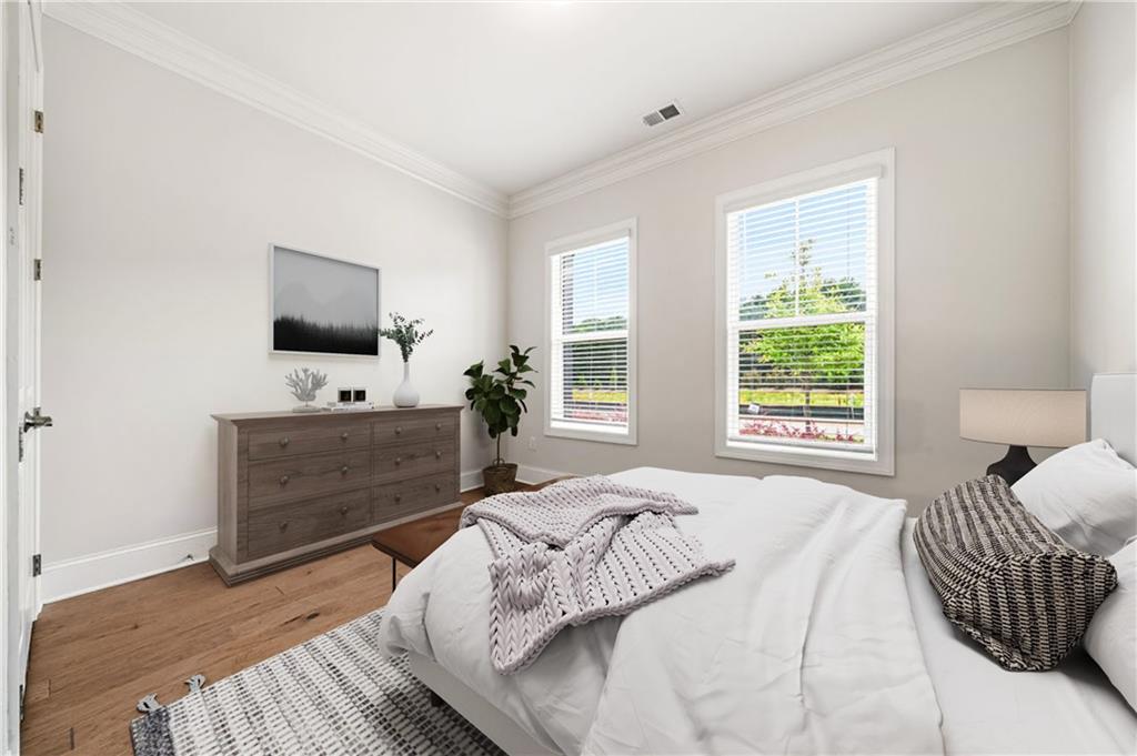 Staged bedroom with a white bed, gray dresser, and two windows overlooking greenery.