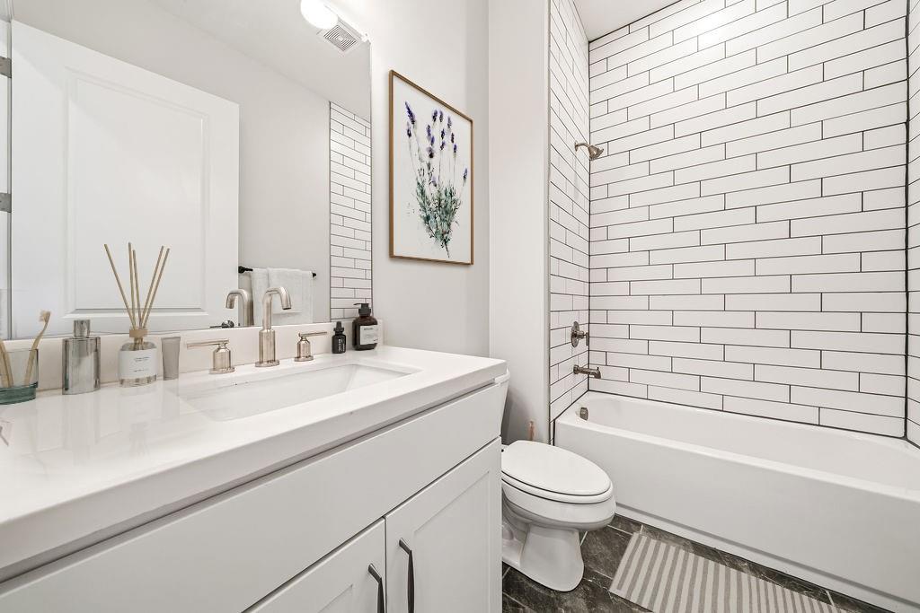 Bathroom with white vanity, toilet, and bathtub lined with white subway tile.