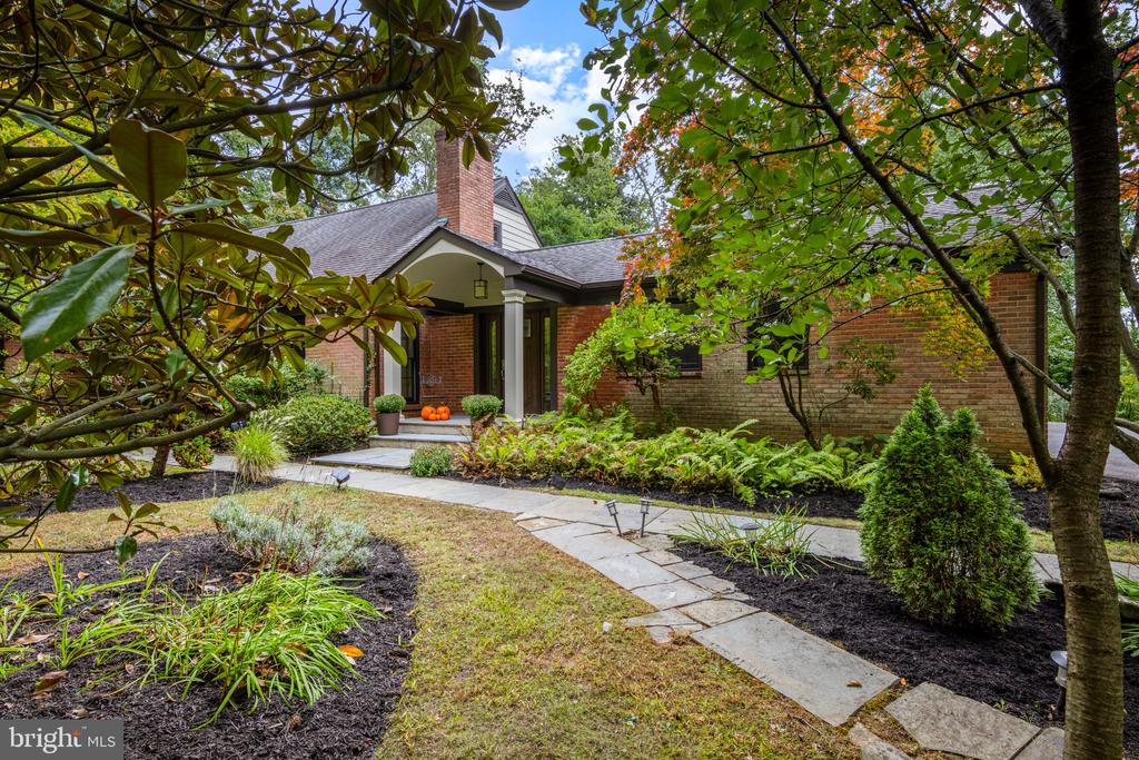 Brick home with a covered entry, mature trees, and a curved stone walkway through landscaped gardens.
