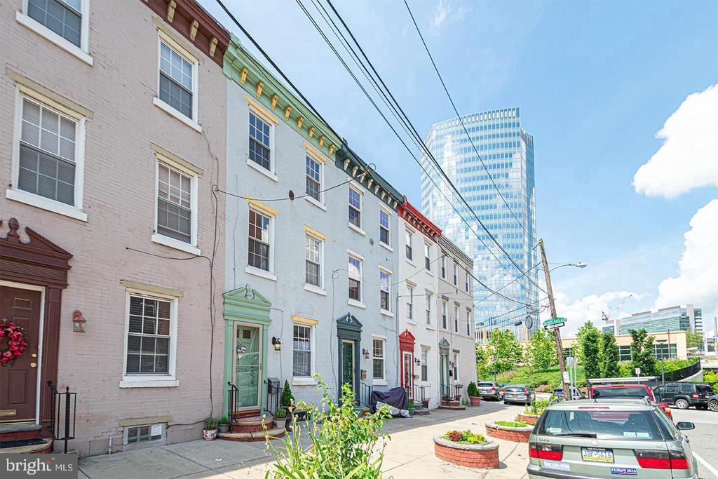 City rowhouses with colorful doors, street parking, and a glass office tower behind them.